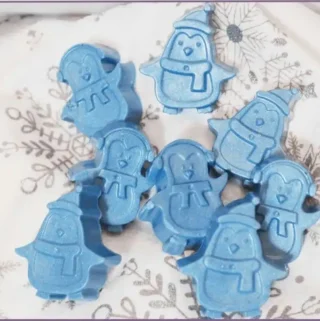 8 blue homemade penguin soap bars on a festive fabric with instructions on how to make them