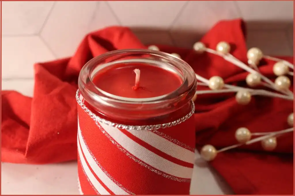 Red candle in a glass jar wrapped with red and white festive fabric - How to make a candy cane candle