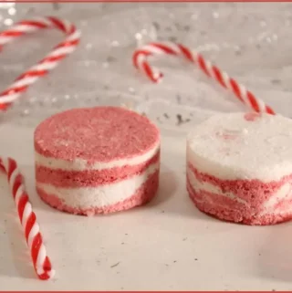 Two round red-and-white layered candy cane bath bombs on a countertop, styled with mini candy canes with instructions on how to make.