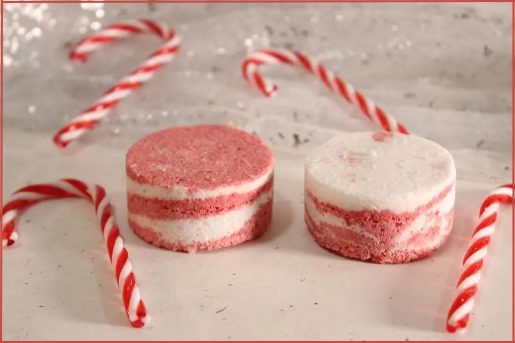 Two round red-and-white layered candy cane bath bombs on a countertop, styled with mini candy canes with instructions on how to make.