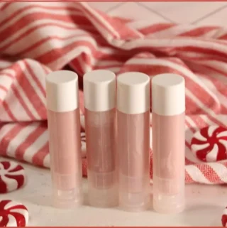 Four DIY candy cane lip balm tubes in front of a red‑and‑white striped towel, with peppermint candies scattered around.