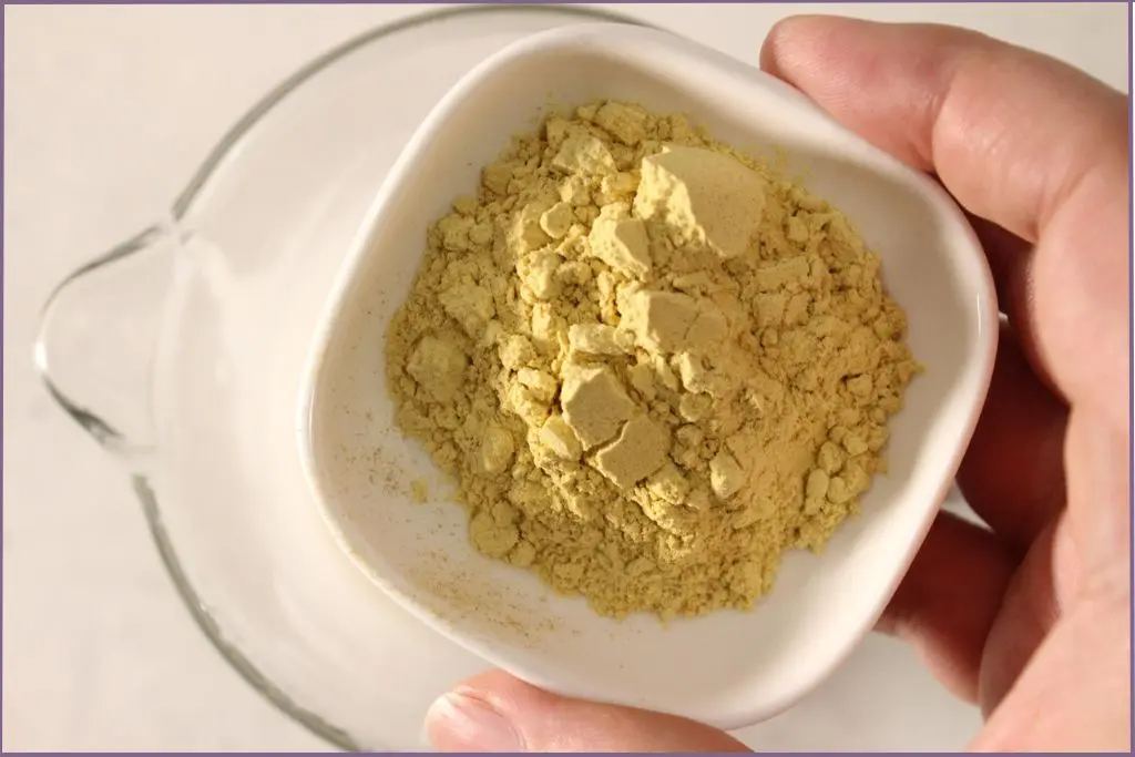 Hand pouring pumpkin powder into melted base to make fall sugar scrub bars