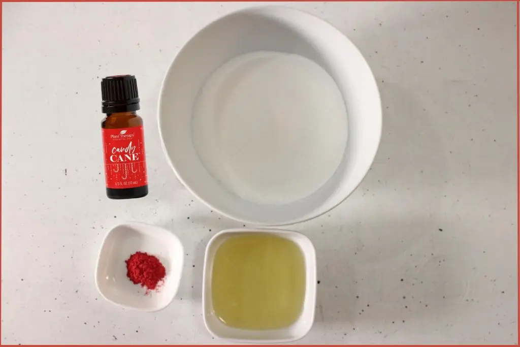 Bowls with white sugar, carrier oil, and mica powder and an essential oil bottle - Candy cane sugar scrub recipe ingredients