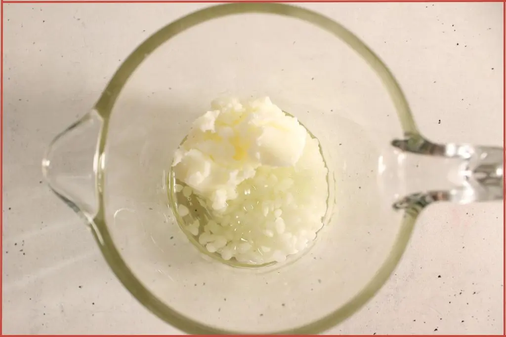 Top view of beeswax, coconut oil, and jojoba oil in a glass measuring jar