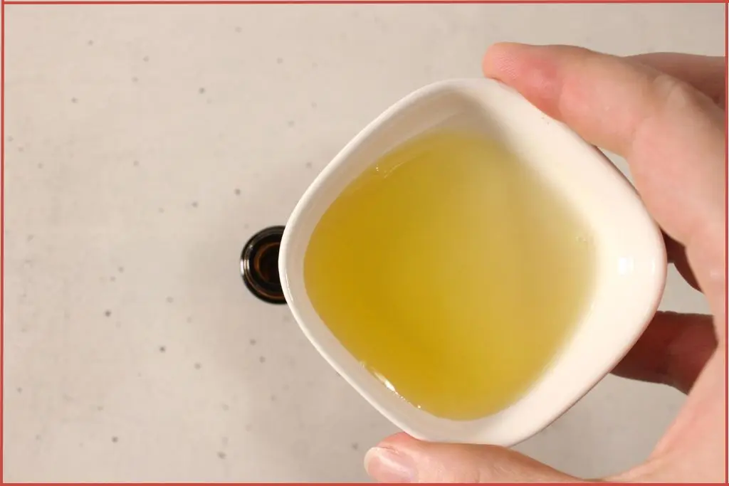 pouring carrier oil and essential oil blend from a white bowl to a roller bottle to make Christmas roll-on perfume