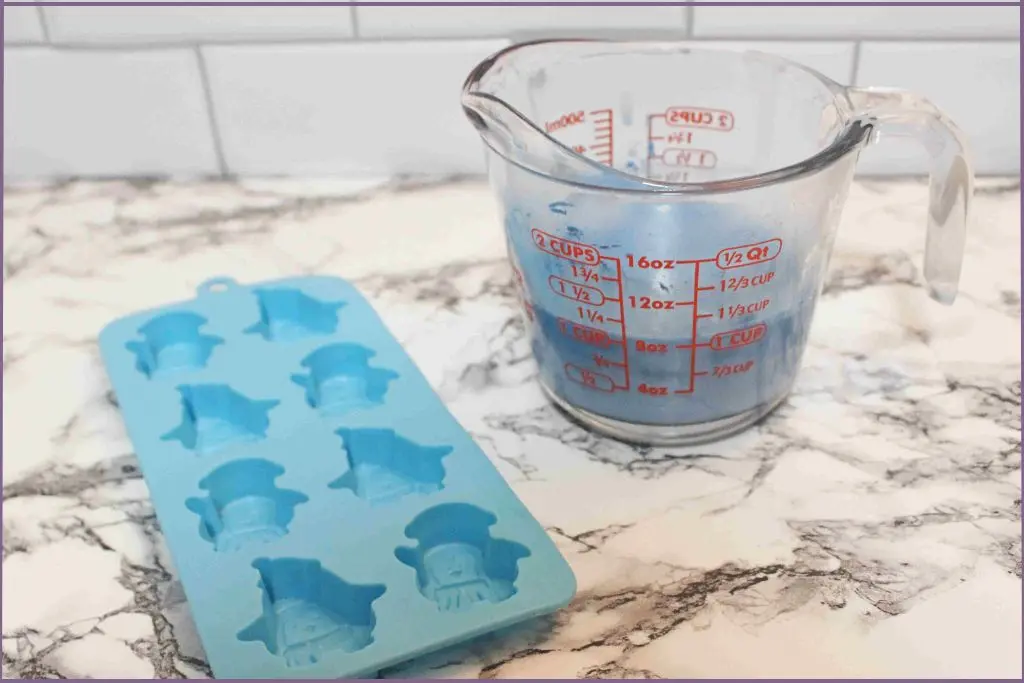 Glass measuring cup with blue melted soap base ready to be poured into penguin shaped soap mold