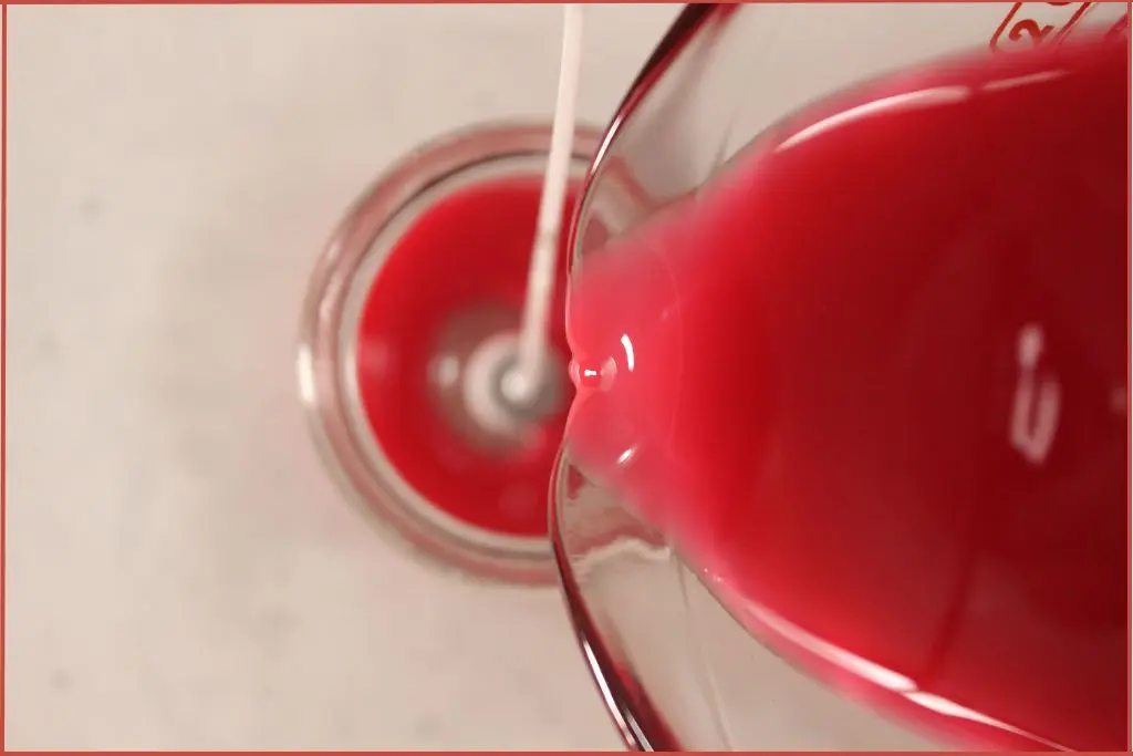 Pouring melted red soy wax into a glass jar to make a candy cane candle