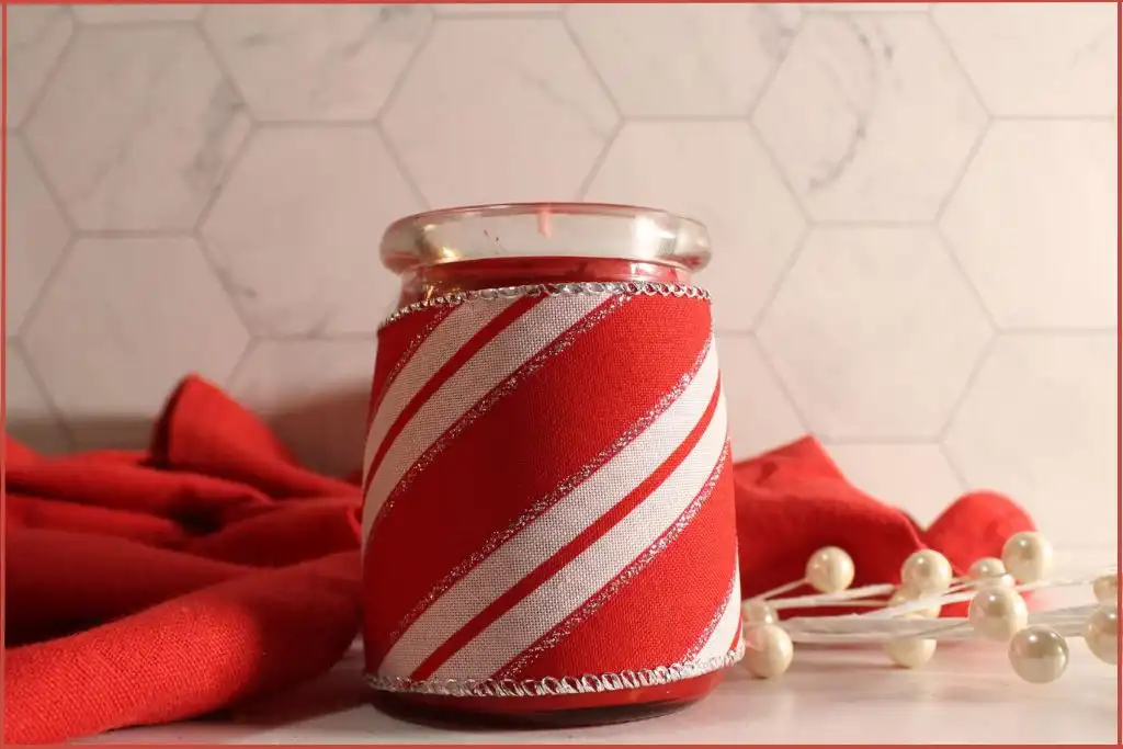 Red candle in a glass jar wrapped with red and white festive fabric cover - precautions when making Christmas candy cane candle