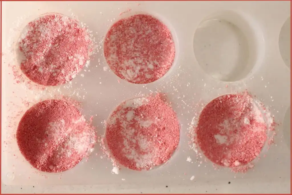 Silicone mold filled with red-and-white bath bomb mixture, showing the packing step of DIY candy cane bath bombs.