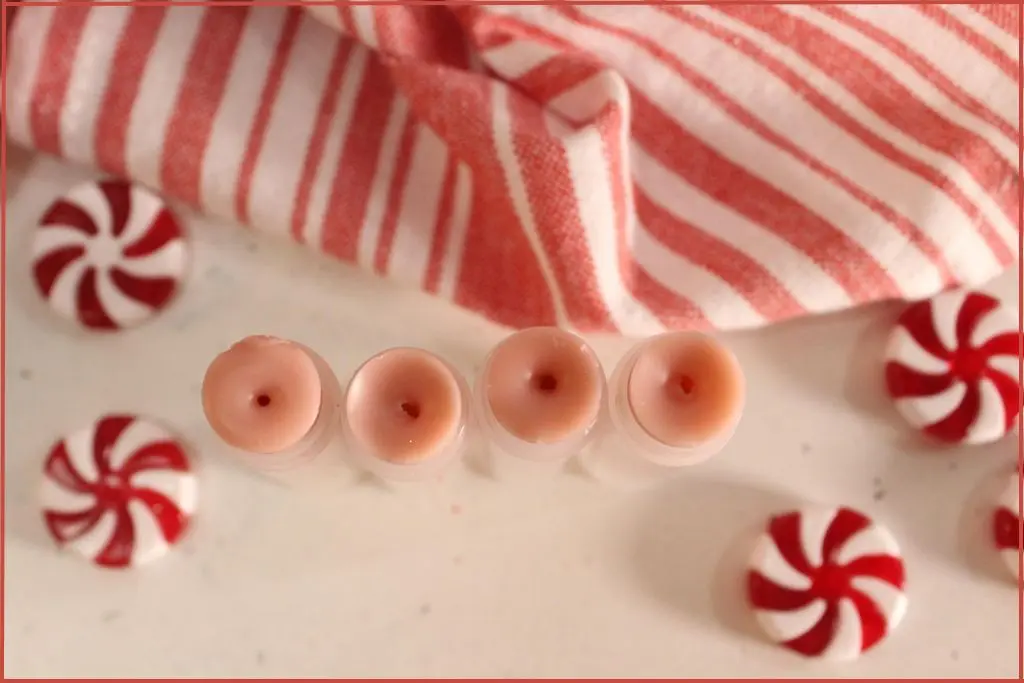 Close‑up of four candy cane lip balms on a counter, surrounded by peppermint candies and a striped towel.