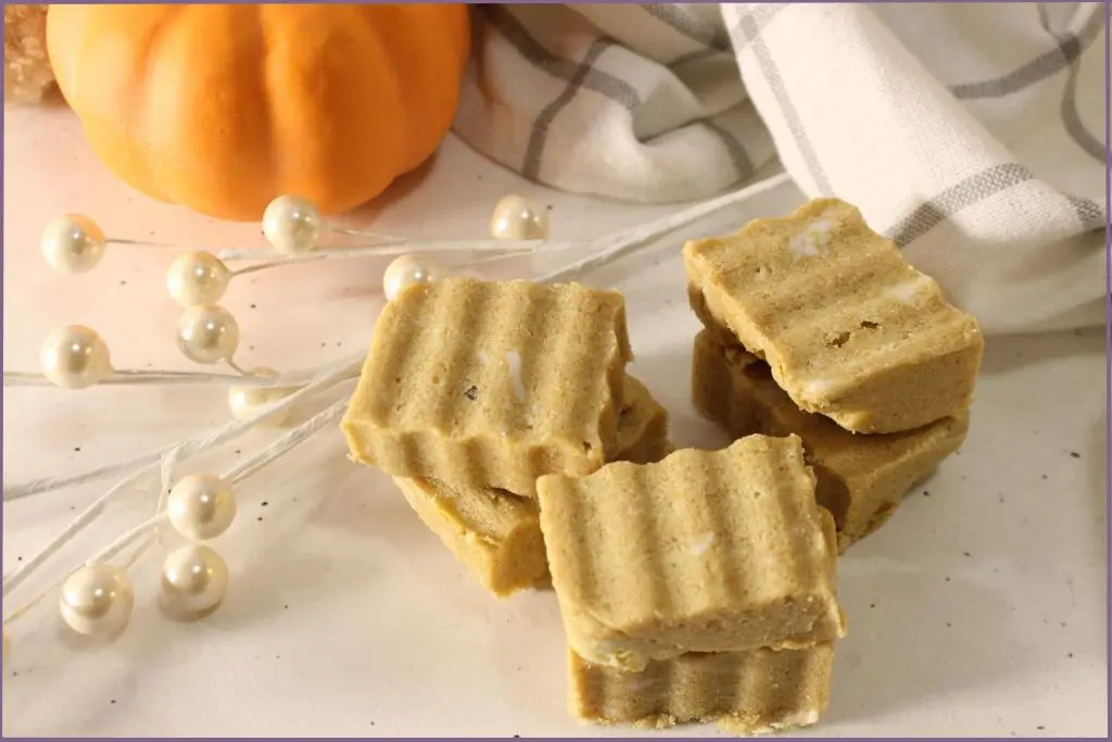 6 Rectangular homemade pumpkin spice sugar scrub bars with ridged tops arranged on a white surface, styled with a plaid kitchen towel, small orange pumpkin, and cozy pumpkin decor with trouble-shooting tips for perfect pumpkin spice sugar scrub bars.