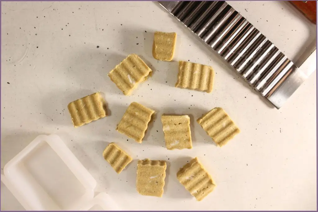 Rectangular homemade pumpkin spice sugar scrub bars with ridged tops lying beside a ridged soap cutter and rectangular soap mold