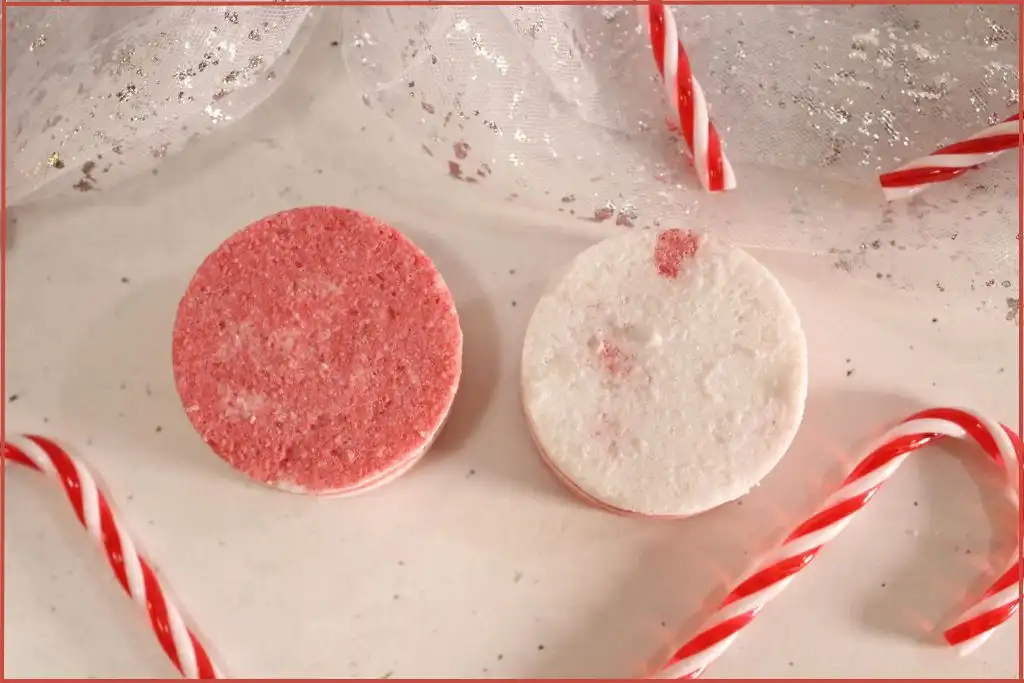 Two round red-and-white layered candy cane bath bombs on a countertop, styled with mini candy canes with instructions on how to make.