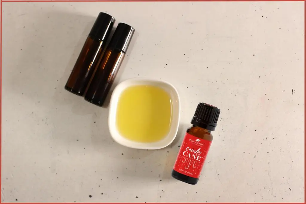 Ingredients for DIY Christmas roll-on perfume - two roll-on bottles, a bowl of carrier oil, and a bottle of candy cane essential oil blend