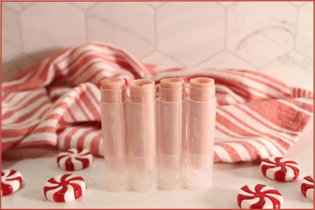Four opened candy cane lip balms on a counter, surrounded by peppermint candies and a striped towel.