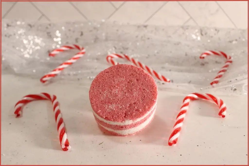 One round red-and-white layered candy cane bath bomb on a countertop, styled with mini candy canes.