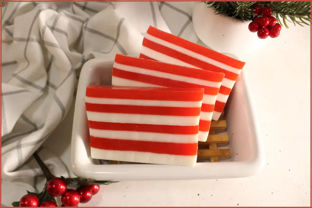 3 red and white striped candy cane soap bars on a wooden tray in a ceramic bowl with red berry decorations for gift packaging ideas