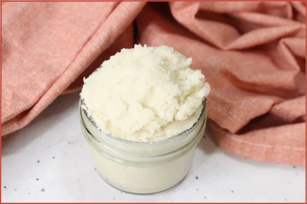 Ivory color sugar scrub in a glass jar surrounded by pink fabric