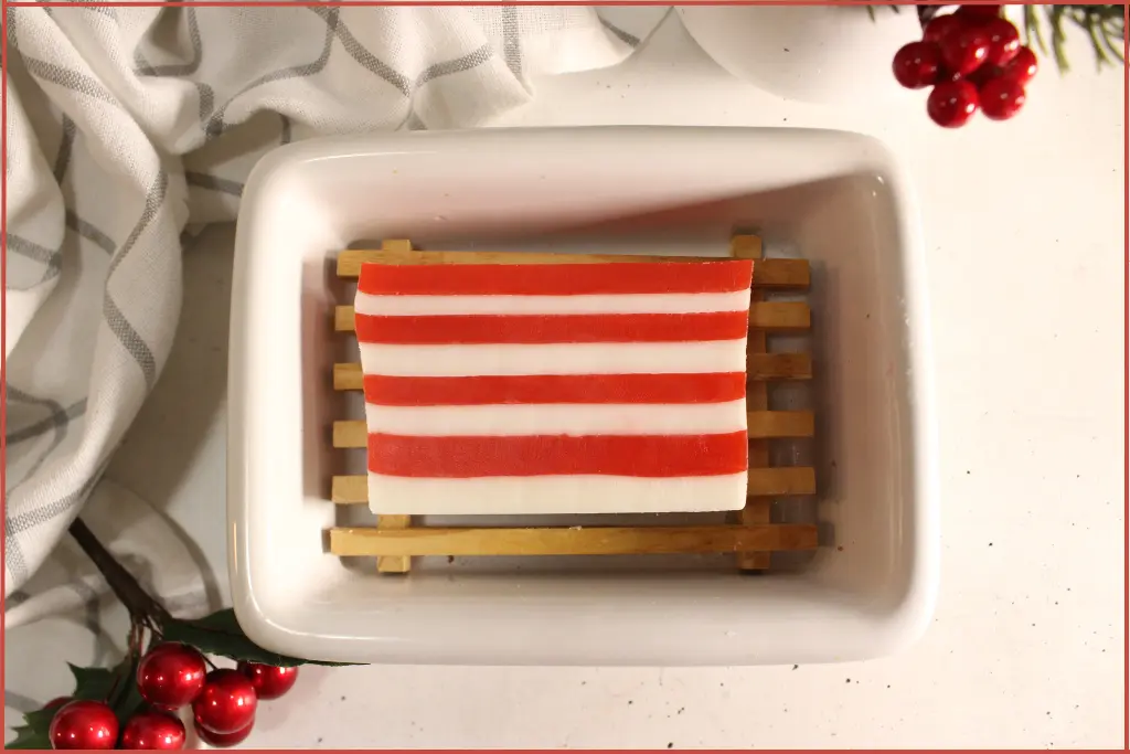 One red and white striped candy cane soap bar on a wooden tray in a ceramic bowl with red berry decorations and ideas for customization