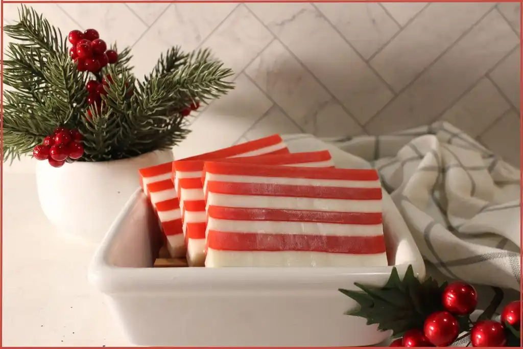 3 red and white striped candy cane soap bars on a wooden tray in a ceramic bowl with Christmas decorations at the side with storage tips