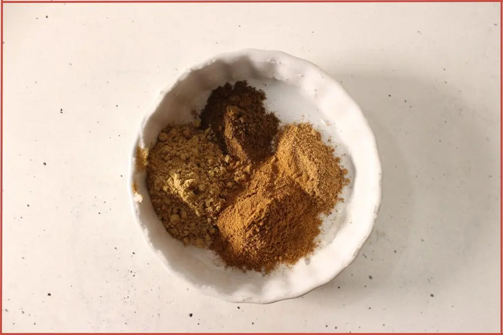4 gingerbread sugar scrub powdered spices - ginger, cinnamon, clove, and nutmeg - in a small white bowl