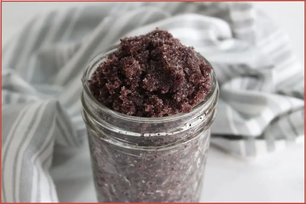 Deep purple color mulled wine sugar scrub in a glass jar surrounded by grey and white striped fabric