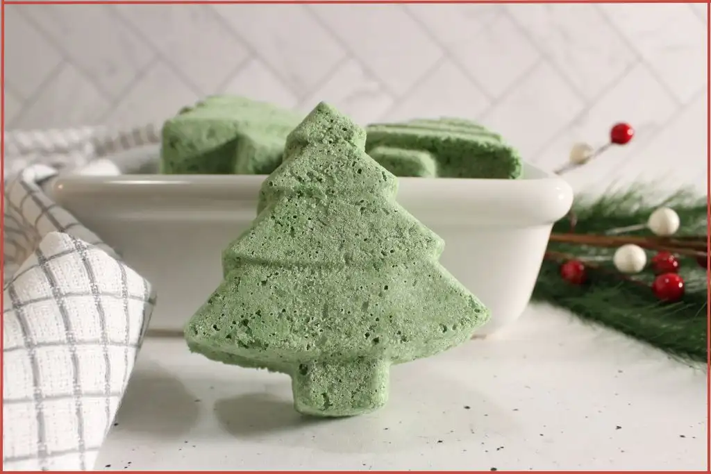 Christmas tree–shaped bath bomb standing upright in front of a dish of more bombs, illustrating texture and firmness after molding.