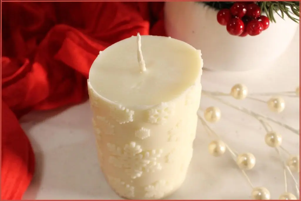 DIY white snowflake pillar candle, styled on a white counter with a red cloth and berries in the background.
