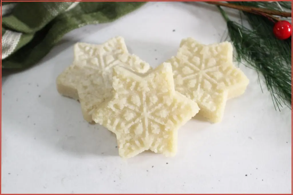 Three white snowflake-shaped sugar scrub bars on a marble surface with evergreen and ribbon, DIY recipe with troubleshooting tips