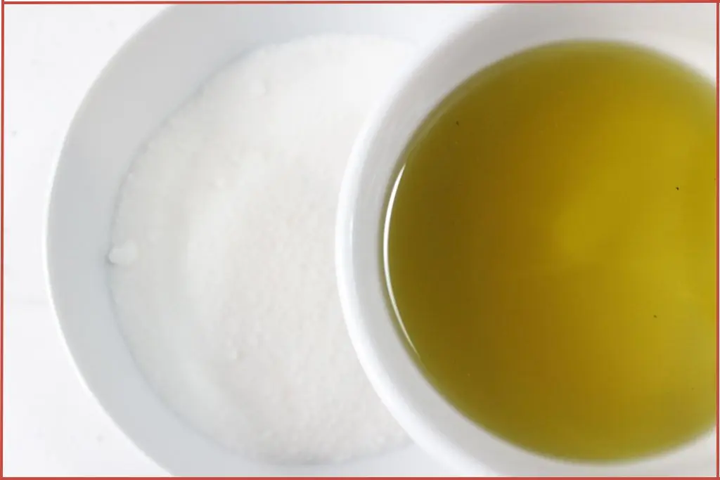 Pouring carrier oil and essential oil blend from a small bowl into a larger bowl of white sugar