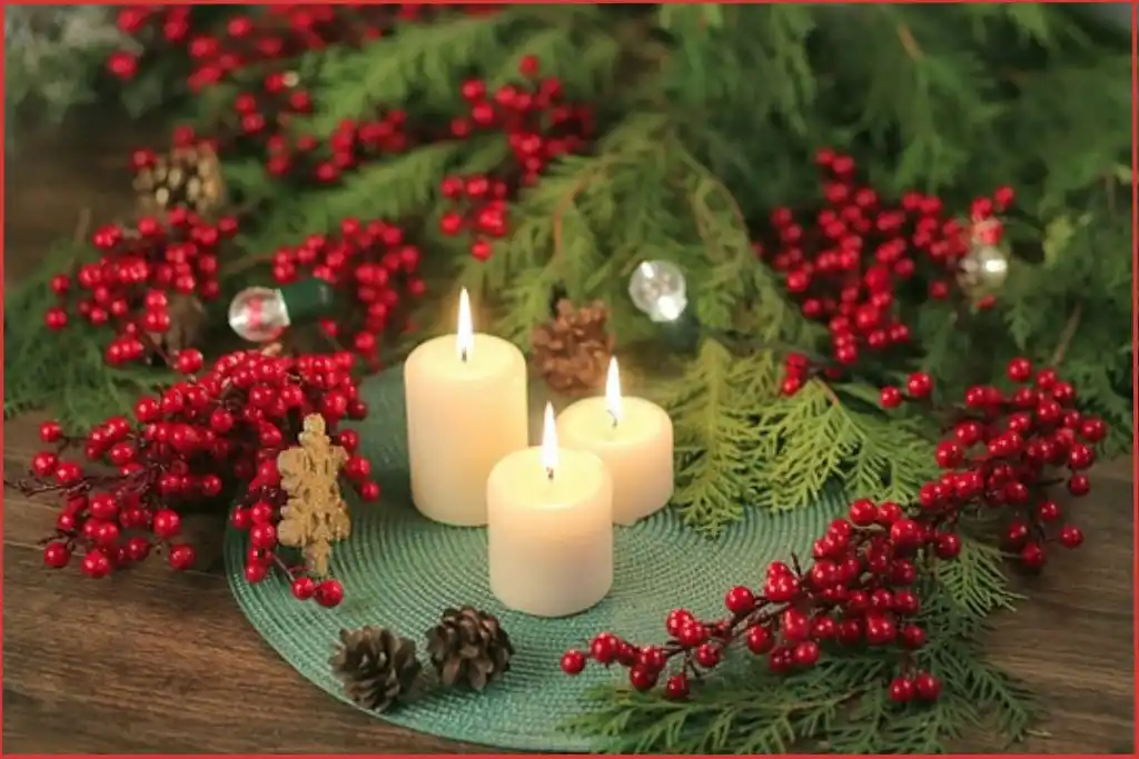Three white pillar candles on a round green placemat with pine leaves and red berries in the background