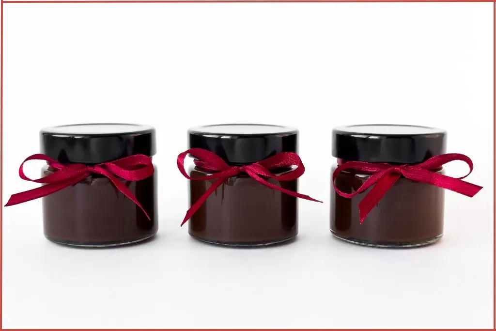 3 dark colored jars with festive red ribbon for gifting Christmas hand cream