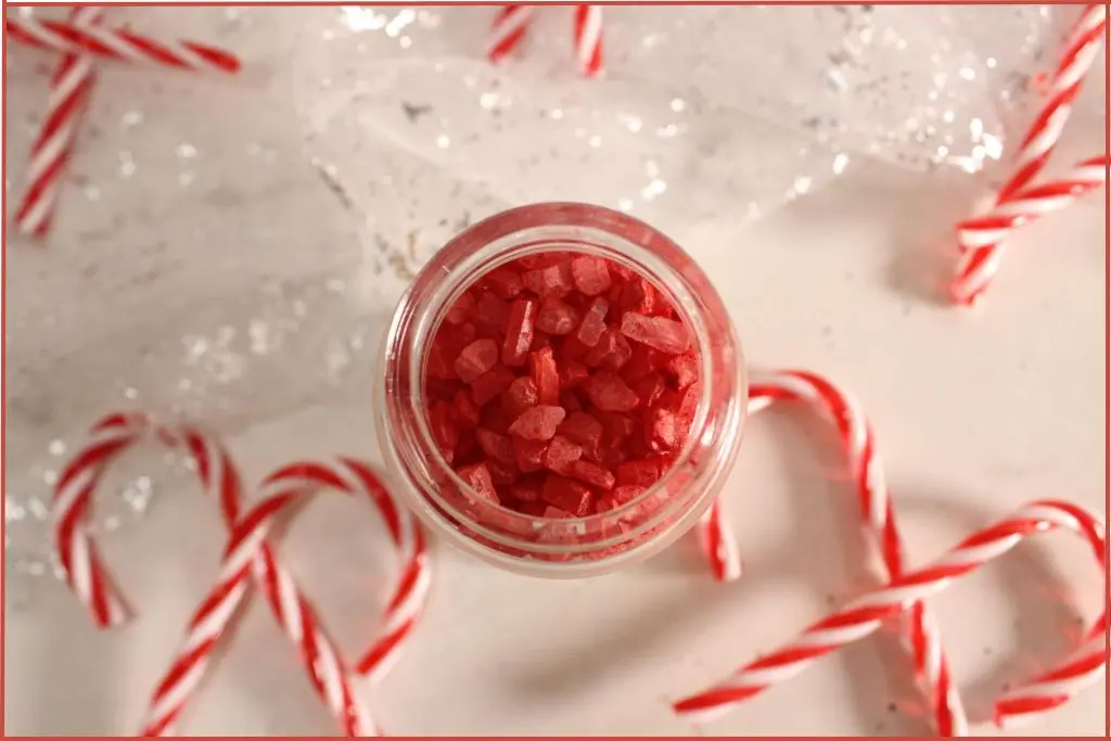 Overhead view of homemade candy cane bath salts, surrounded by striped candy canes on a white, sparkly background.