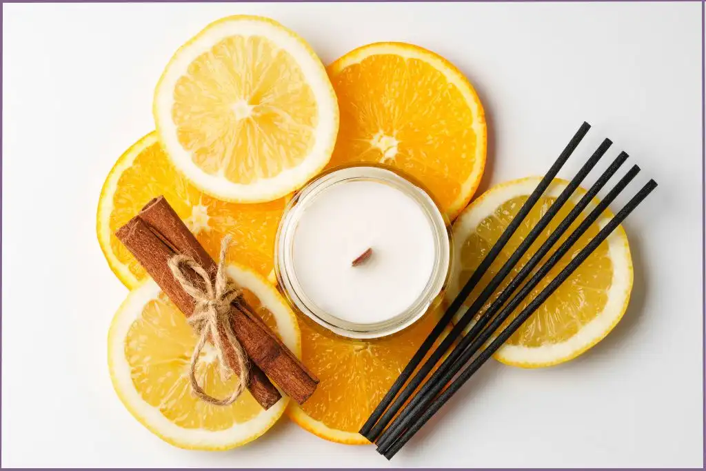 small white candle in holder sitting on top of citrus slices, bundle of cinnamon sticks, and reed sticks