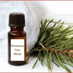 Bottle of Christmas tree essential oil blend in front of a rolled up white towel and fir needles