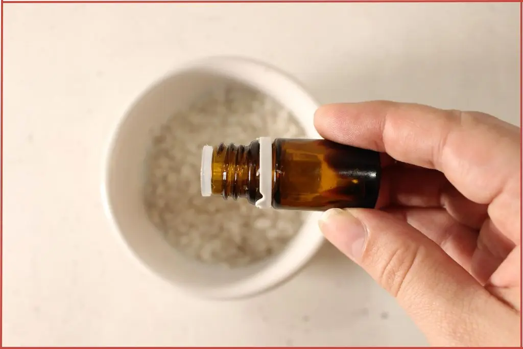 Hand pouring essential oil into a bowl of Dead Sea salt to make candy cane bath salts