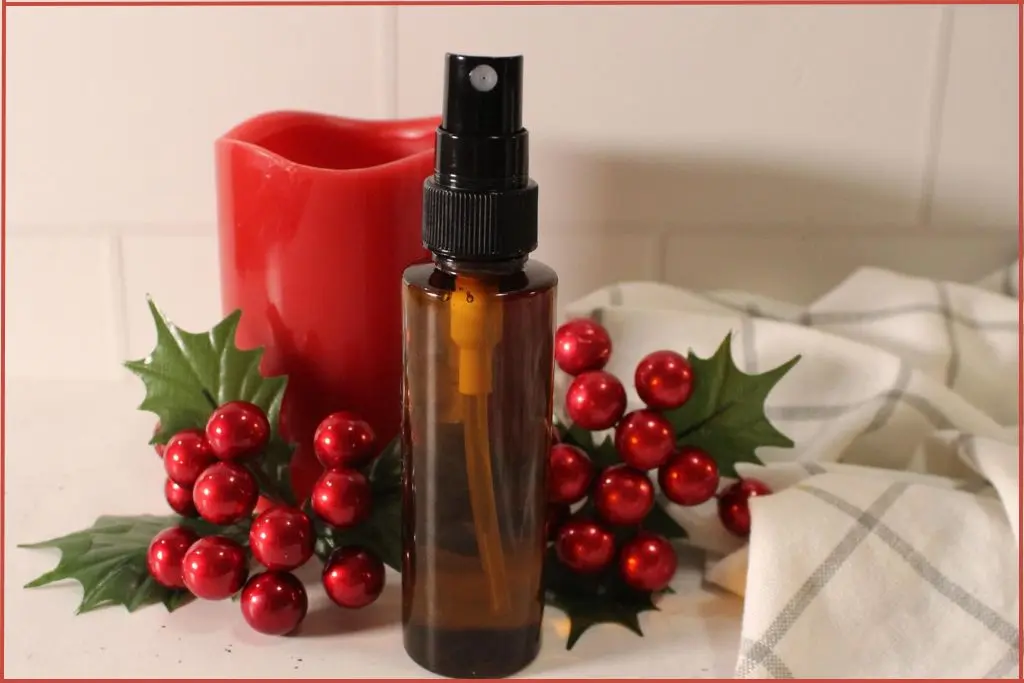 amber color glass spray bottle in front of red Christmas berries and candle.